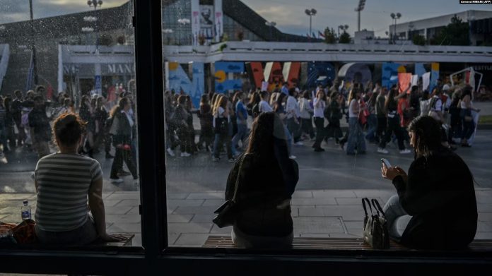 Disa gra në një stacion autobusi ndërsa në rrugë njerëzit marshojnë gjatë një proteste në Prishtinë, më 15 prill 2024, pas vrasjes së një gruaje 21-vjeçare.